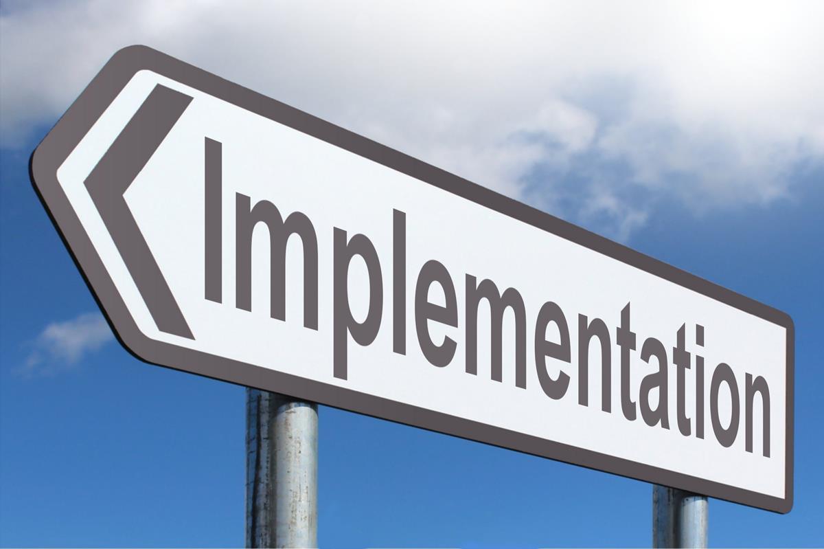  A road sign with the word "Implementation" pointing to the left against a blue sky and white clouds background representing the search query 'Cloudbased application implementation'.